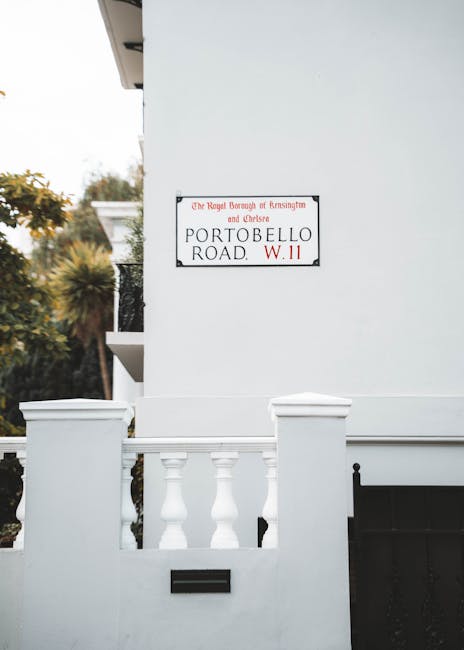 Two movers from Chelsea Movers are preparing for a home relocation outside a storefront with Chinese characters and the word 'GUANGH' visible above the entrance. One mover, standing to the left, holds