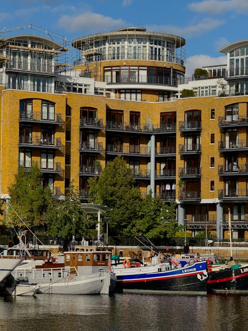 Aerial view of Chelsea Harbour in London during sunset, featuring a marina with several rows of moored boats and yachts, surrounded by modern residential buildings with balconies. The scene includes a